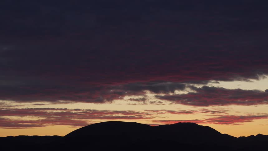 Vibrant red and purple clouds stretch across the sky at sunset over silhouetted mountains