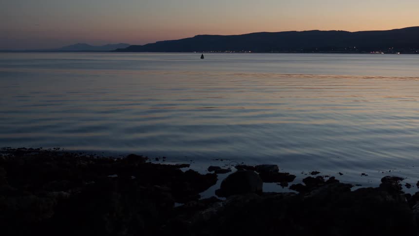 Tranquil coastal scene at dusk with calm water and distant hills