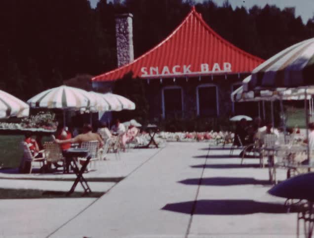 Many tables with umbrellas sit by a snack bar