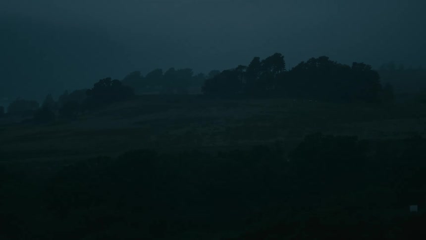 Dark misty landscape with silhouetted trees on a hill at dusk