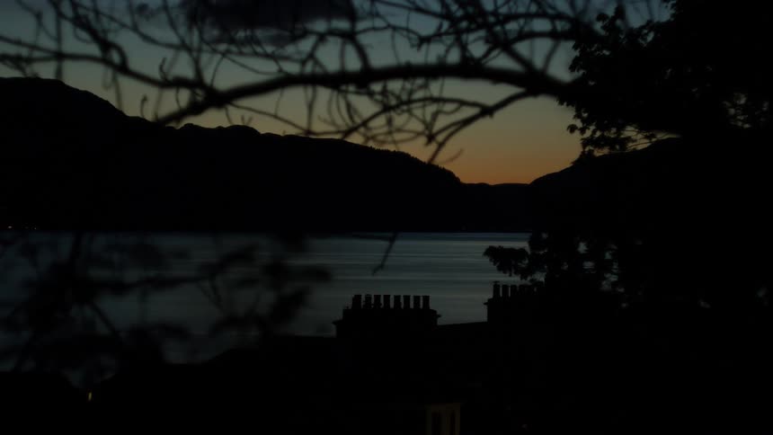 Silhouetted village by a lake at dusk framed by bare branches