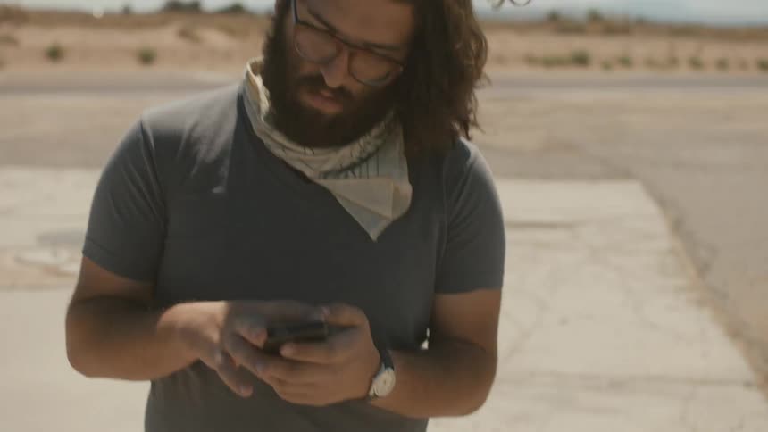 A man checks his phone while standing in the wind
