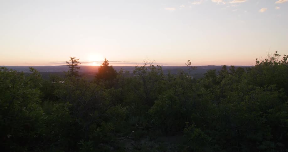 Sun sets behind hills over a dense forest