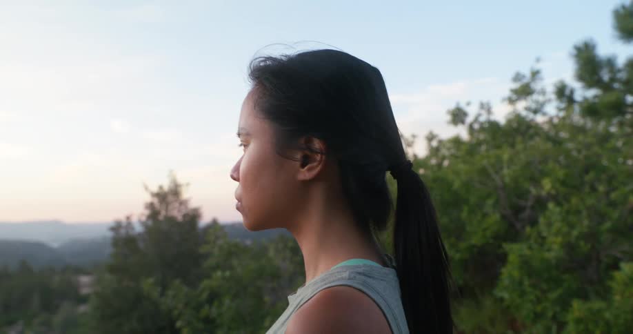 A young woman stands on a cliff in the jungle catching her breath after a run at midday