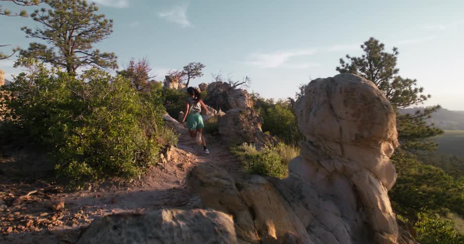 A woman jogs along a rocky forest trail in the golden light of late afternoon