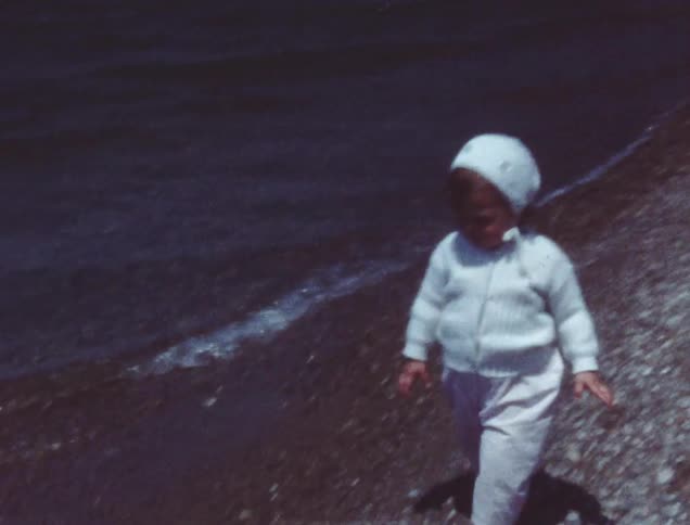 A toddler girl walks on a lakeshore