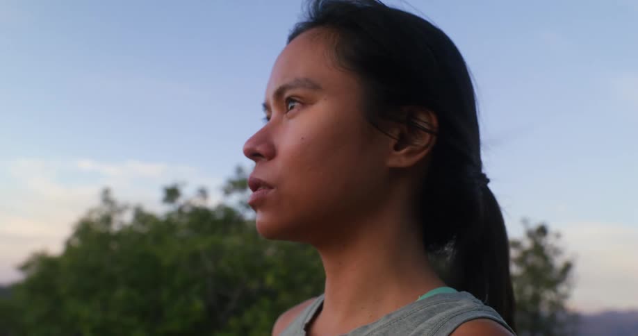 A young woman stands atop a mountain and takes a deep breath