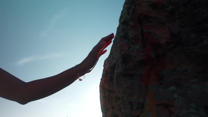 The woman reaches out and puts her palm on the boulder