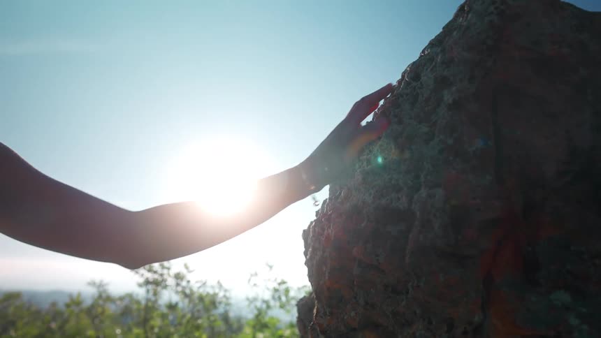 A person places their hand on a sunlit rock