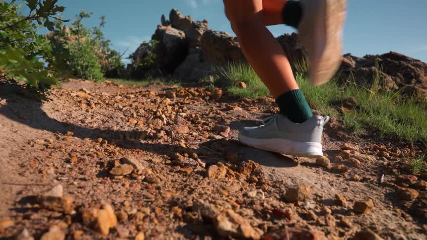 A young woman runs up a hill on rocky terrain at midday