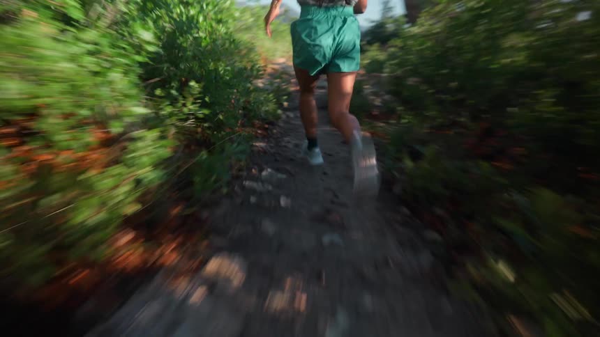 A female with very long hair is running fast on a trail outdoors