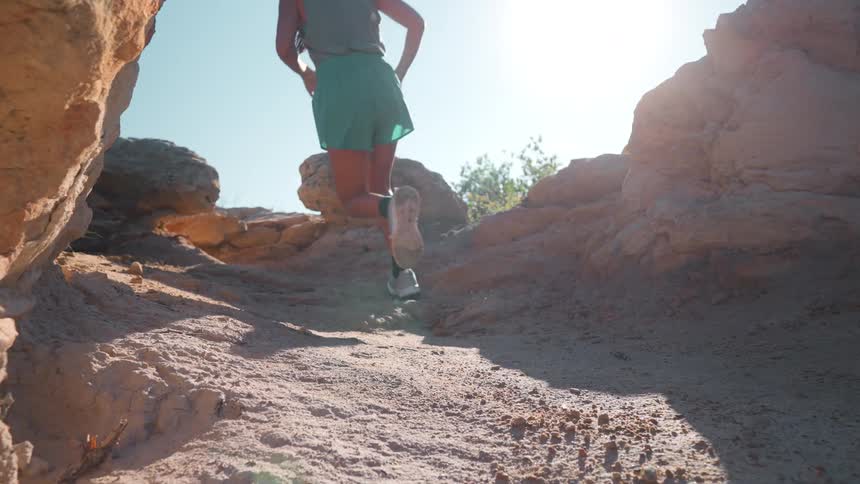 Woman is running uphill on a trail with the bright sun shining on her