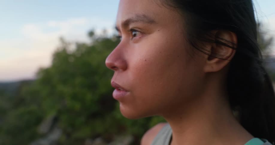 A young woman stands on a mountain cliff catching her breath after a run at midday