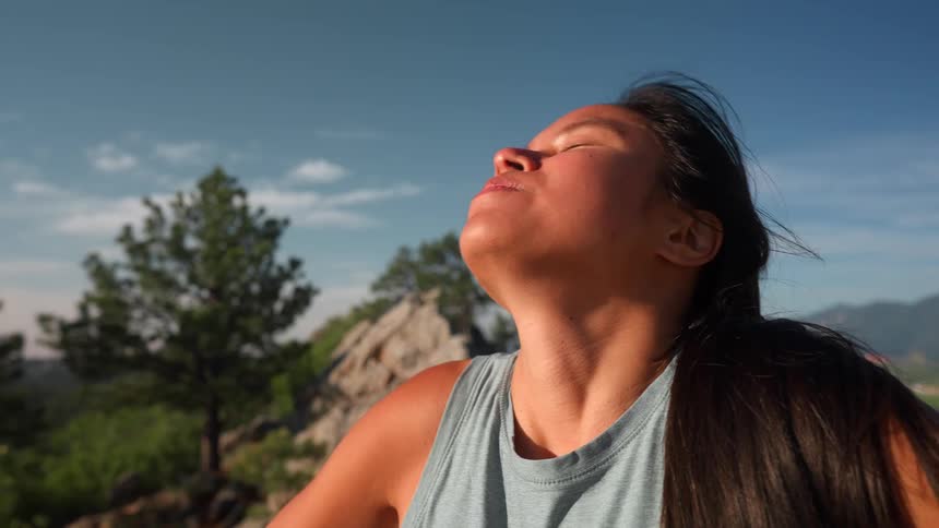 Woman taking deep breaths while standing on a mountain during the day