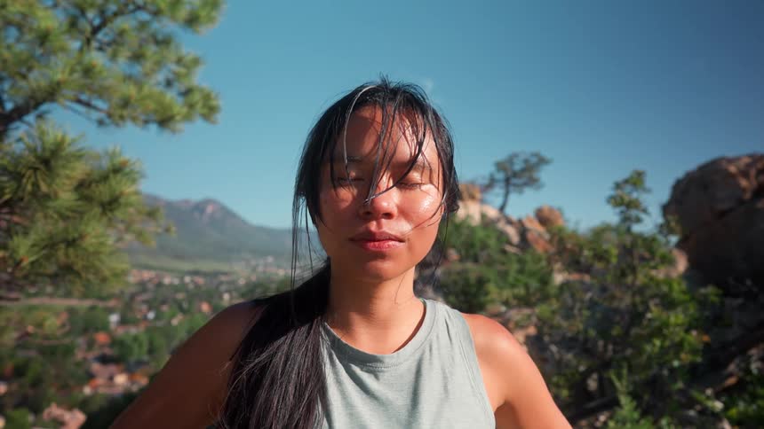 An asian female is standing outdoors breathing heavy with her eyes closed