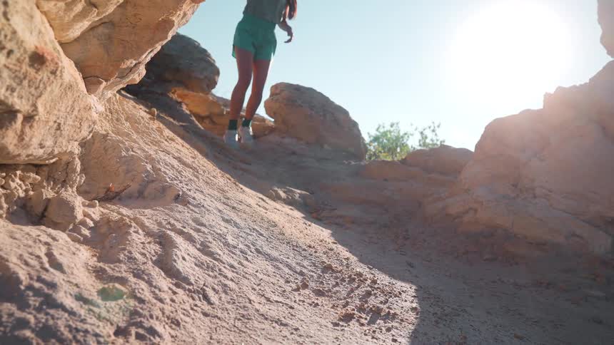 In slow motion a runner descends a rocky sun drenched trail