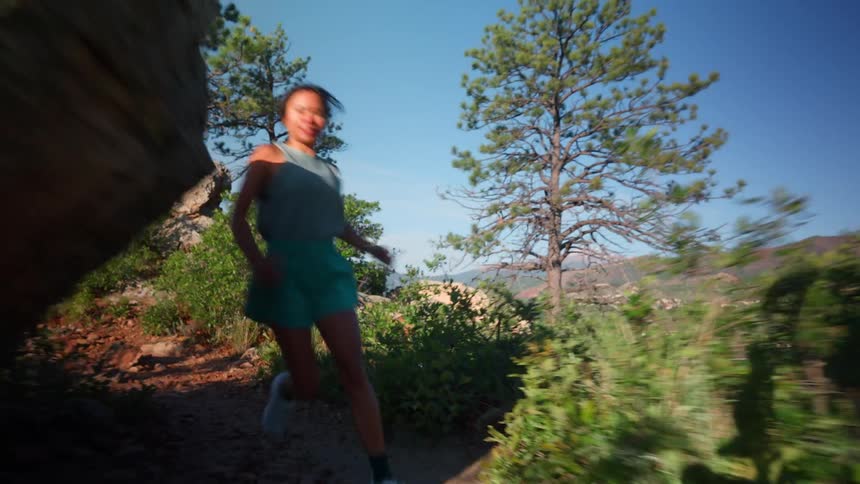 A woman running on a land with trees and rocks at midday