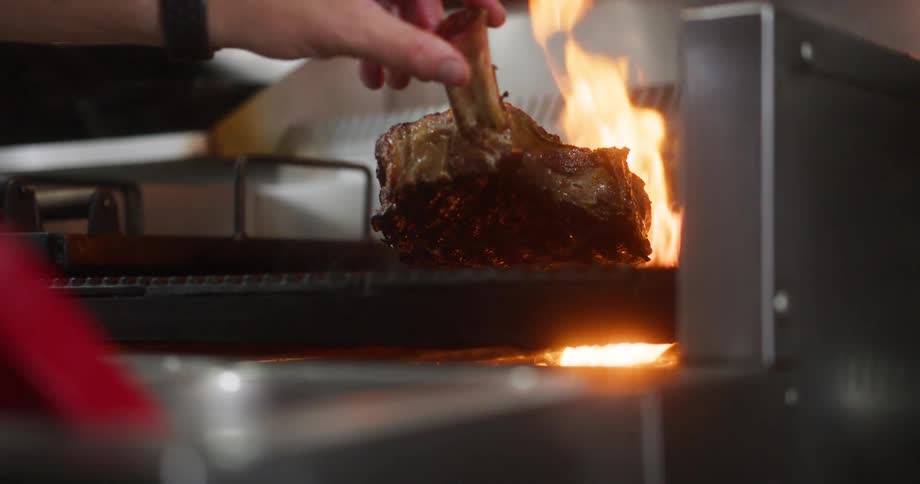The cook puts the steak on the grill with fire rising