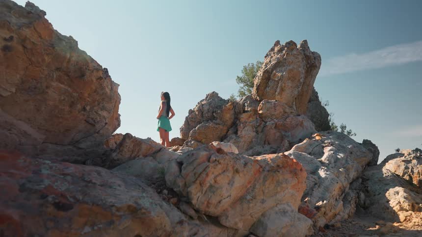 Woman looks up at the sun at the peak of the mountain