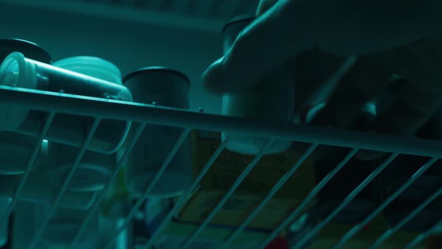 A hand reaches into a dimly lit refrigerator stocked with rolls of film