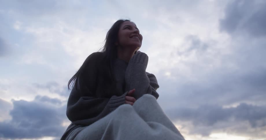 A woman is smiling and sitting under a cloudy sky