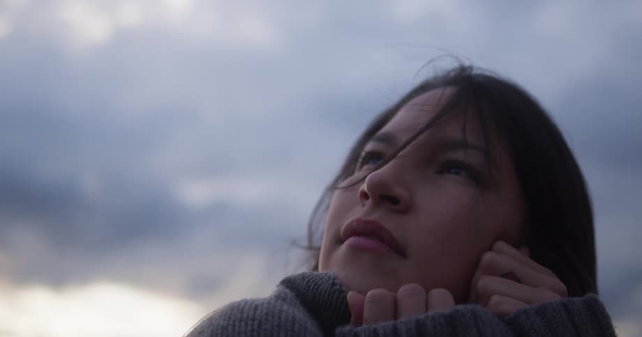 A female is standing outside wearing a sweater holding her hands to her face