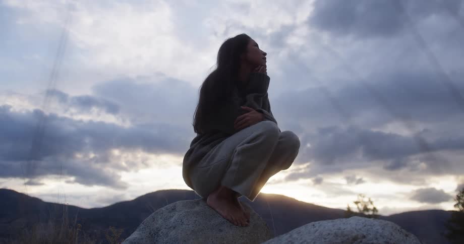 Barefoot woman crouching on top of a rock outdoors