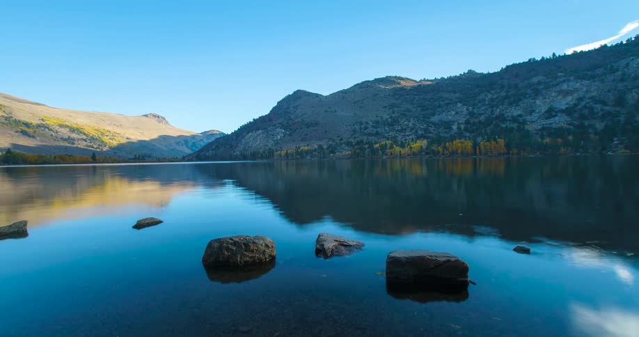 A timelapse captures the sun rising over a serene Silver Lake in the Sierra Nevada mountains with the calm water perfectly reflecting the sky and surrounding autumn landscape