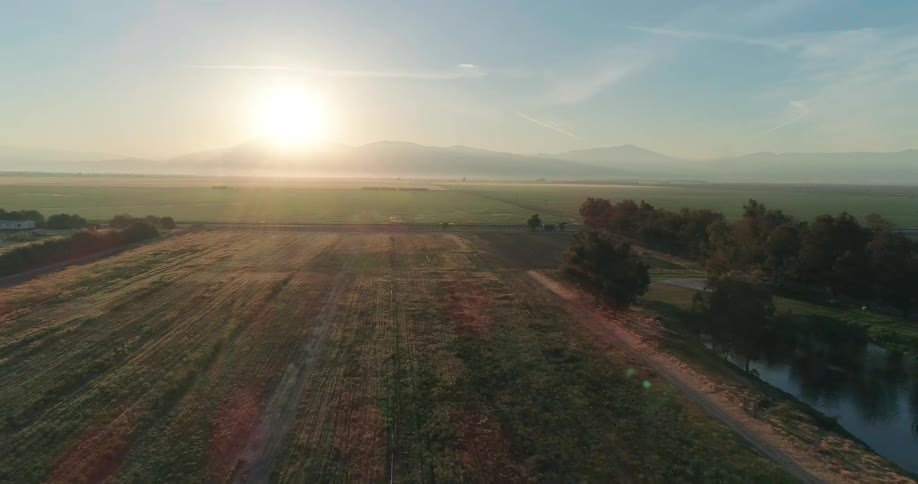 Aerial view of a sunlit rural landscape at dawn with open fields and distant mountains
