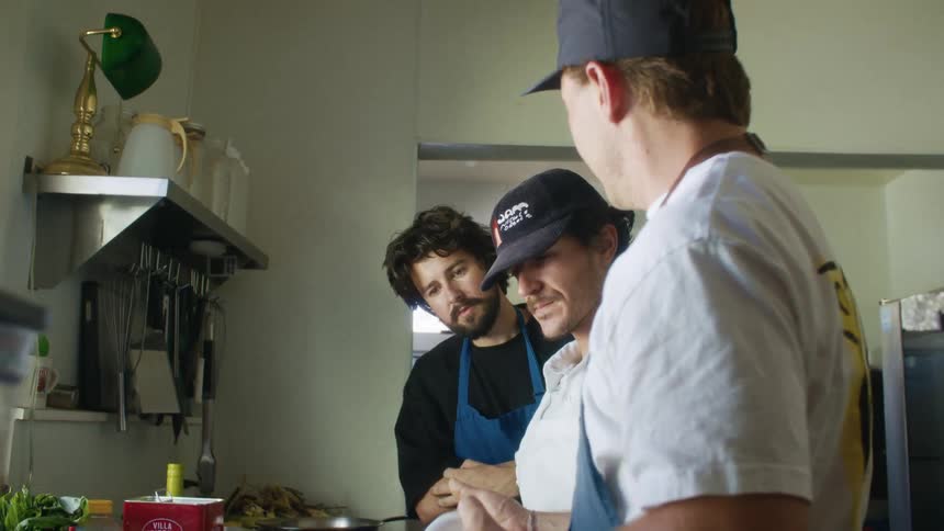 Three men in aprons talking and cooking