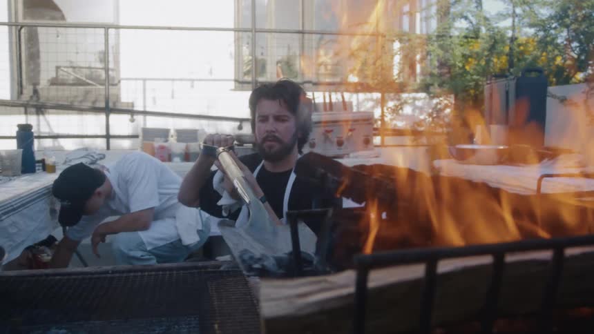 Man grilling over open flame with long handled tool