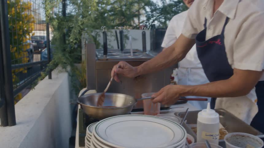 Chef stirs sauce in a pan at an outdoor cooking station