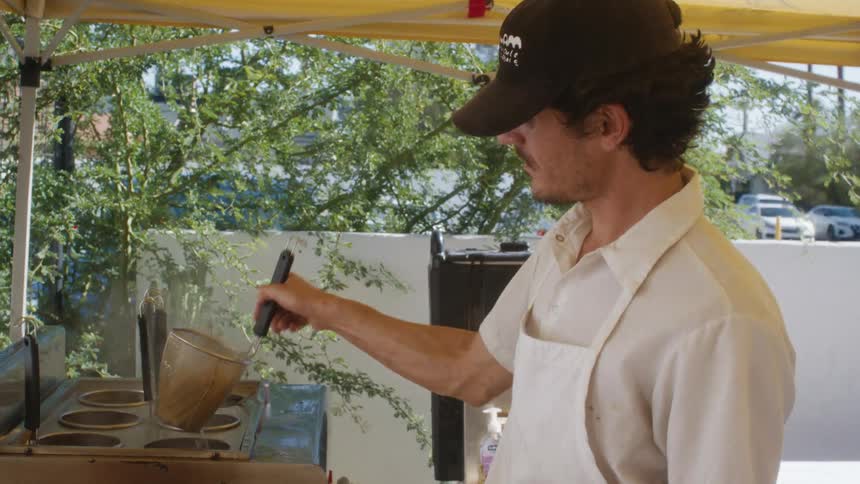 A chef cooks food in a pan over a gas burner at an outdoor food station
