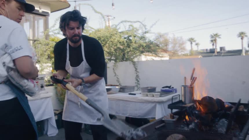 A man shovels charcoal out of the grill