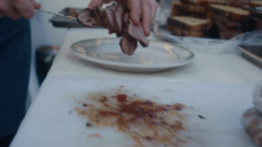 Person slices cooked meat onto a plate at a food prep station