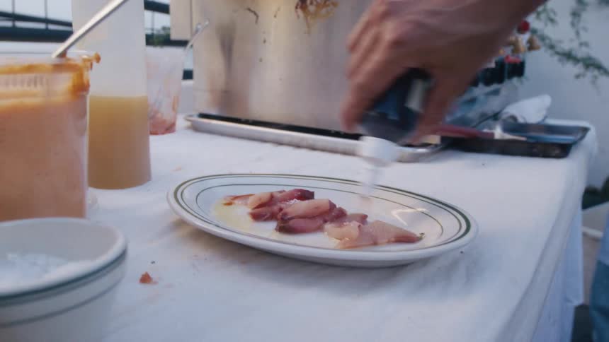 Close up of a male chef pouring sauce from a bottle around a plated dish on a table