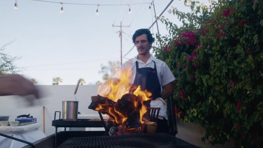 Chefs tend a blazing outdoor grill under string lights