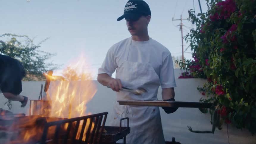 A man grills food over open flames at an outdoor setup
