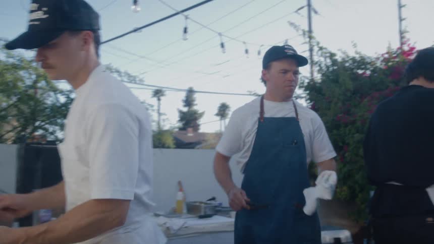 Three men in aprons cooking in an outdoor kitchen