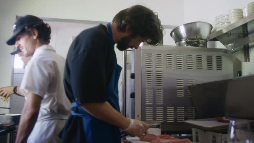 Three chefs in a restaurant kitchen with one of them cutting fish