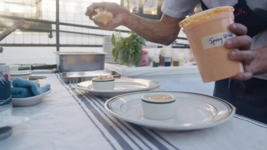 A chef spoons spicy sauce into small bowls on plates during food preparation