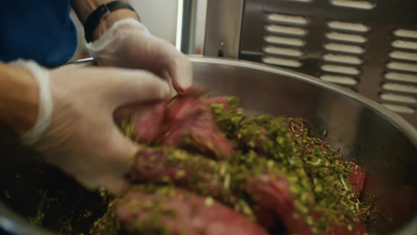 White gloved hands mixing seasonings into meat in a large metal bowl