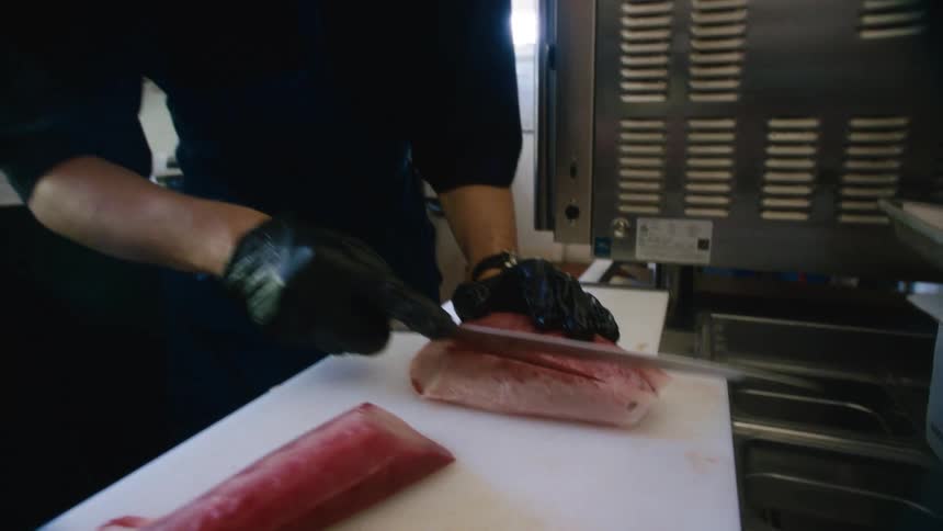 Man in apron and gloves cutting a slice of meat and carefully