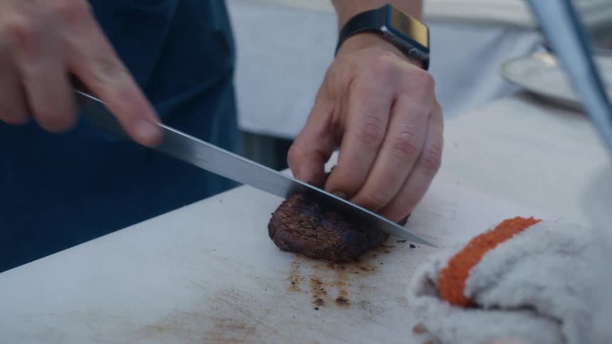 A person slices cooked meat on a cutting board in a closeup kitchen scene