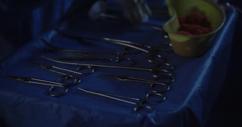 Pair of gloved hands of a healthcare professional handling scalpels on a medical table