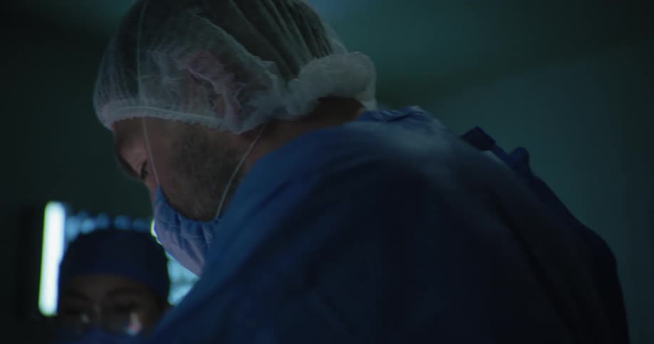 Three doctors clean up blood with tissue from an open area on a patients body in the operating theater