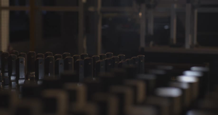 Rows of metal components are lined up in a dimly lit industrial setting suggesting assembly or manufacturing equipment