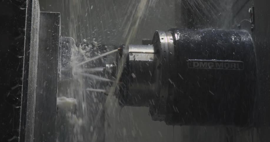 A cnc machine drills into metal while coolant sprays continuously