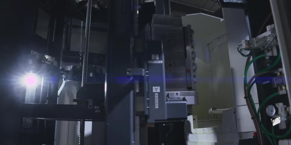 A dark metallic industrial machine with multiple components and wires is moving in a low light setting