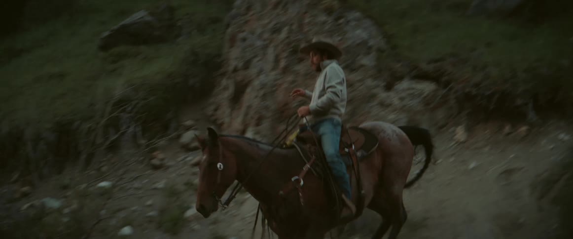 Two men ride horses on rocky terrain as they climb down a hill
